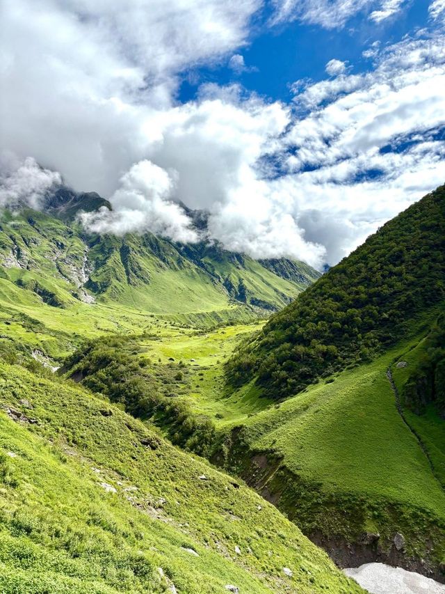 A green valley between steep slopes, with clouds on the ridges